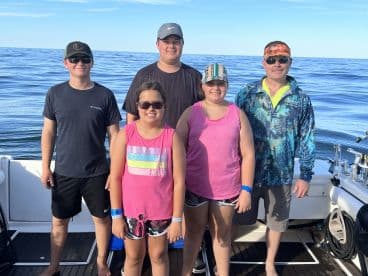 A group of five individuals, including children, posing on a boat with calm waters in the background, likely after a fishing trip.