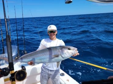 A young angler proudly displaying a large fish while fishing offshore, surrounded by a vibrant blue ocean.