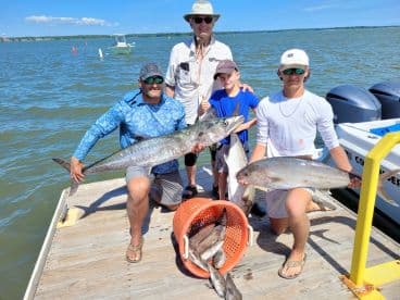 A family proudly displaying their catch of the day, including a large King Mackerel and other fish, at the dock after a successful fishing trip.