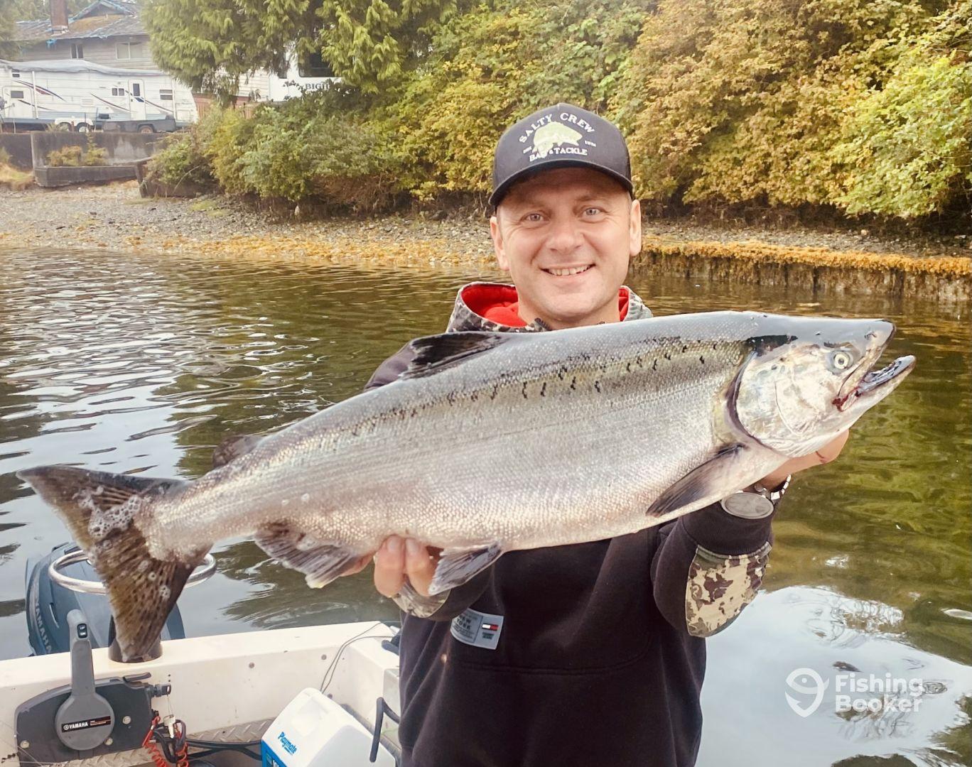 Angler proudly displaying a large Salmon caught while fishing in a scenic coastal area.