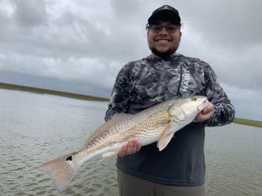 Angler proudly displaying a large Redfish while fishing in a coastal waterway, showcasing a successful catch.