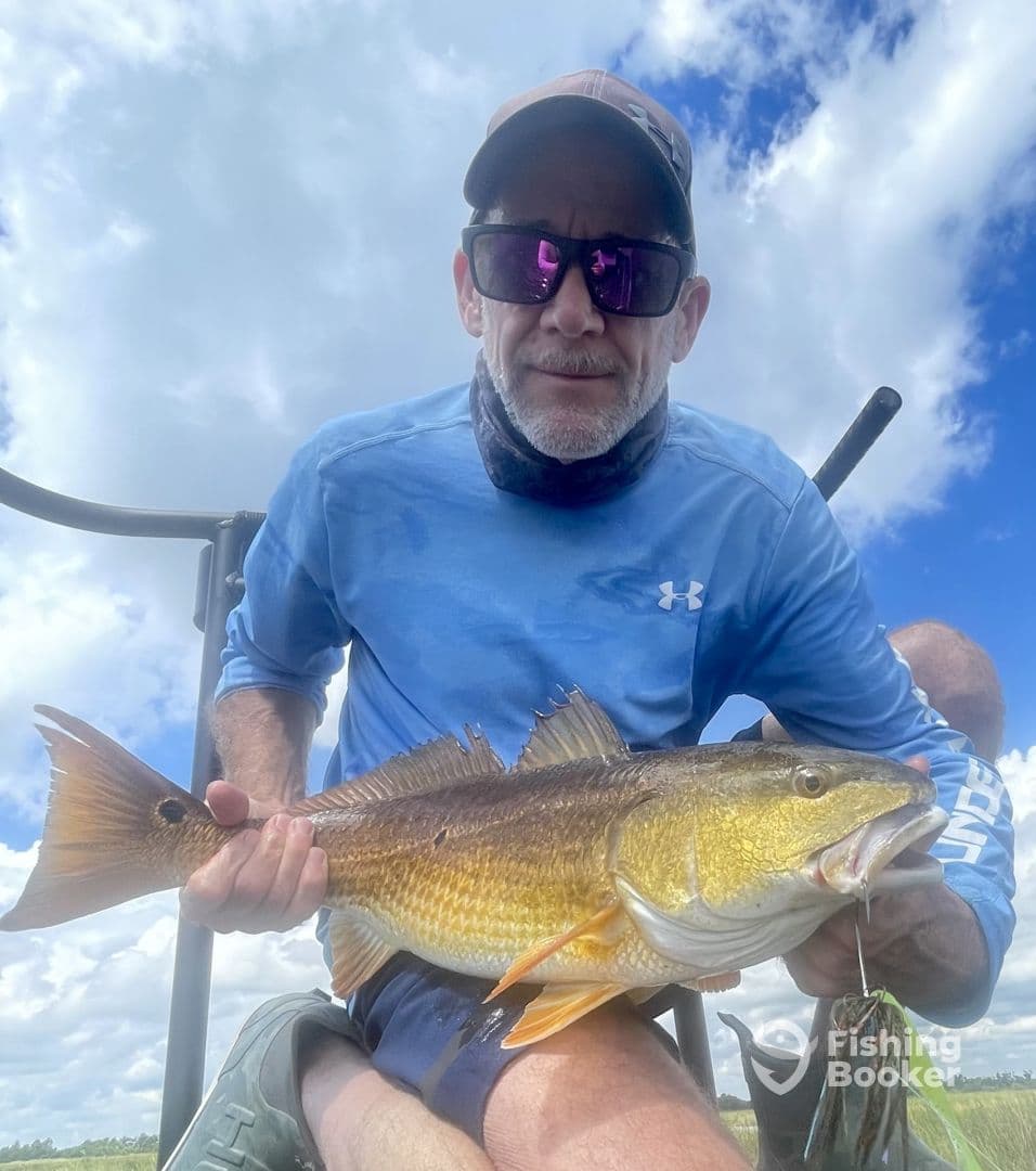 An angler proudly displaying a large Redfish while fishing in a scenic outdoor setting.