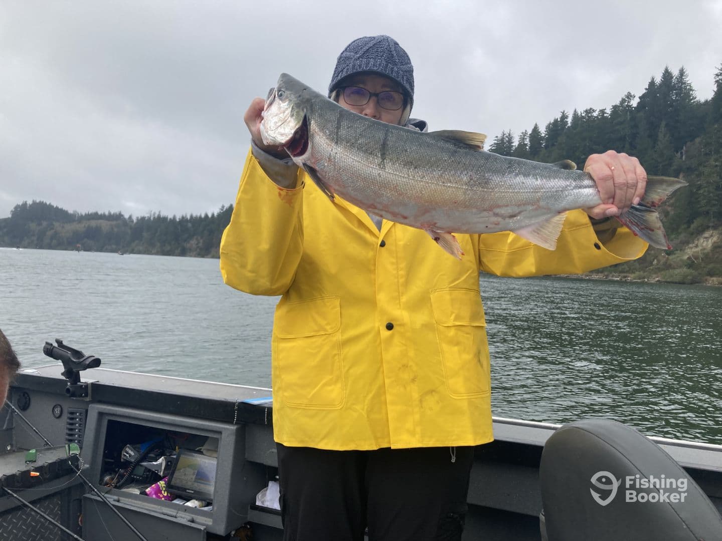 An angler proudly displaying a large Silver Salmon while fishing from a boat in a scenic coastal environment.