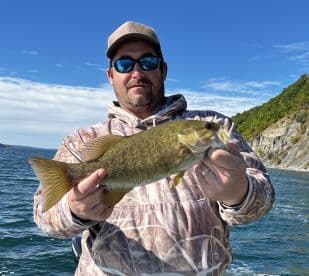 An angler proudly displaying a healthy Smallmouth Bass while fishing on a scenic lake, surrounded by autumn foliage.