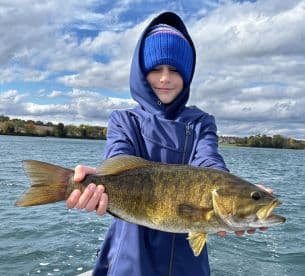 A young angler proudly displaying a large Smallmouth Bass while fishing on a scenic lake, showcasing the excitement of youth fishing adventures.