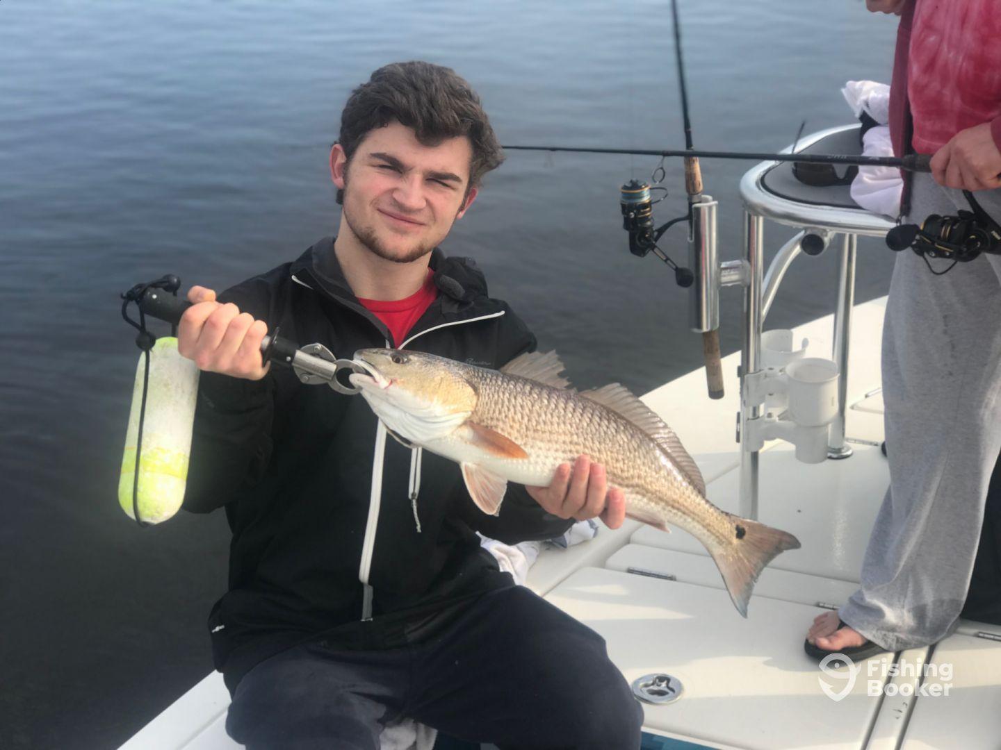 An angler proudly displaying a large Redfish while fishing from a boat, showcasing a successful catch in calm waters.