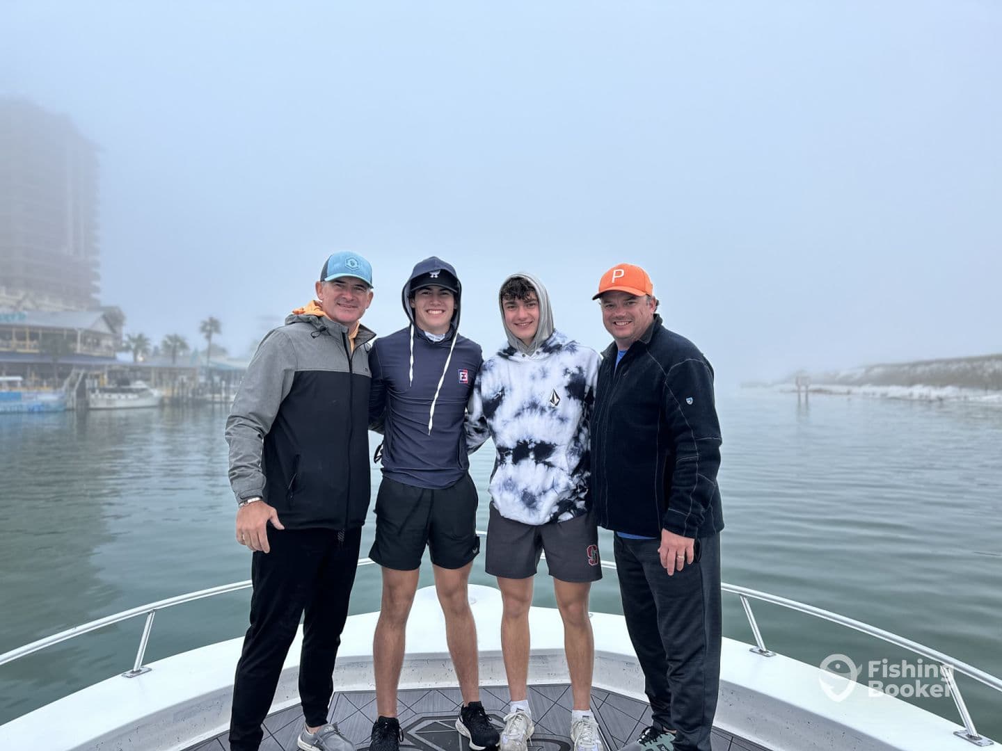Group of four individuals posing on the bow of a boat in foggy conditions, likely preparing for a fishing trip.
