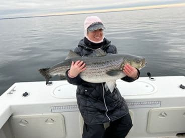 Angler proudly displaying a large striped bass while fishing on a calm water body.