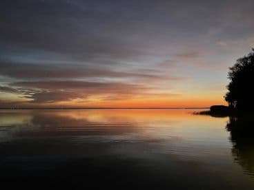 A serene sunset over calm waters, reflecting vibrant colors in the sky, creating a picturesque fishing environment.