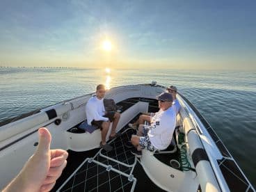 Three anglers relaxing on the boat's interior during a calm morning on the water, with a stunning sunrise in the background.