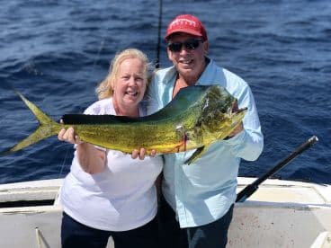 Two anglers proudly displaying a large Mahi Mahi while fishing offshore, showcasing a successful day on the water.