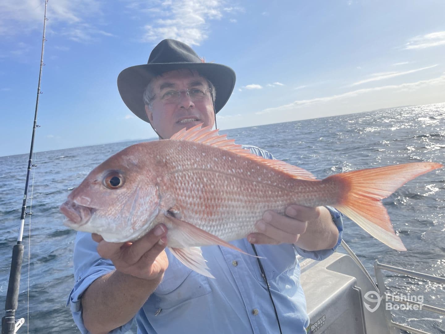 Angler proudly displaying a large Snapper while fishing offshore, showcasing a sunny day on the water.