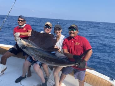 A group of anglers proudly displaying a large Sailfish aboard a sportfishing boat in open waters.