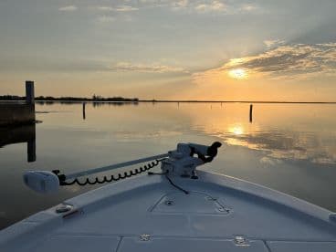 A serene sunset view from the front of a boat, reflecting on calm waters, showcasing a peaceful fishing environment.