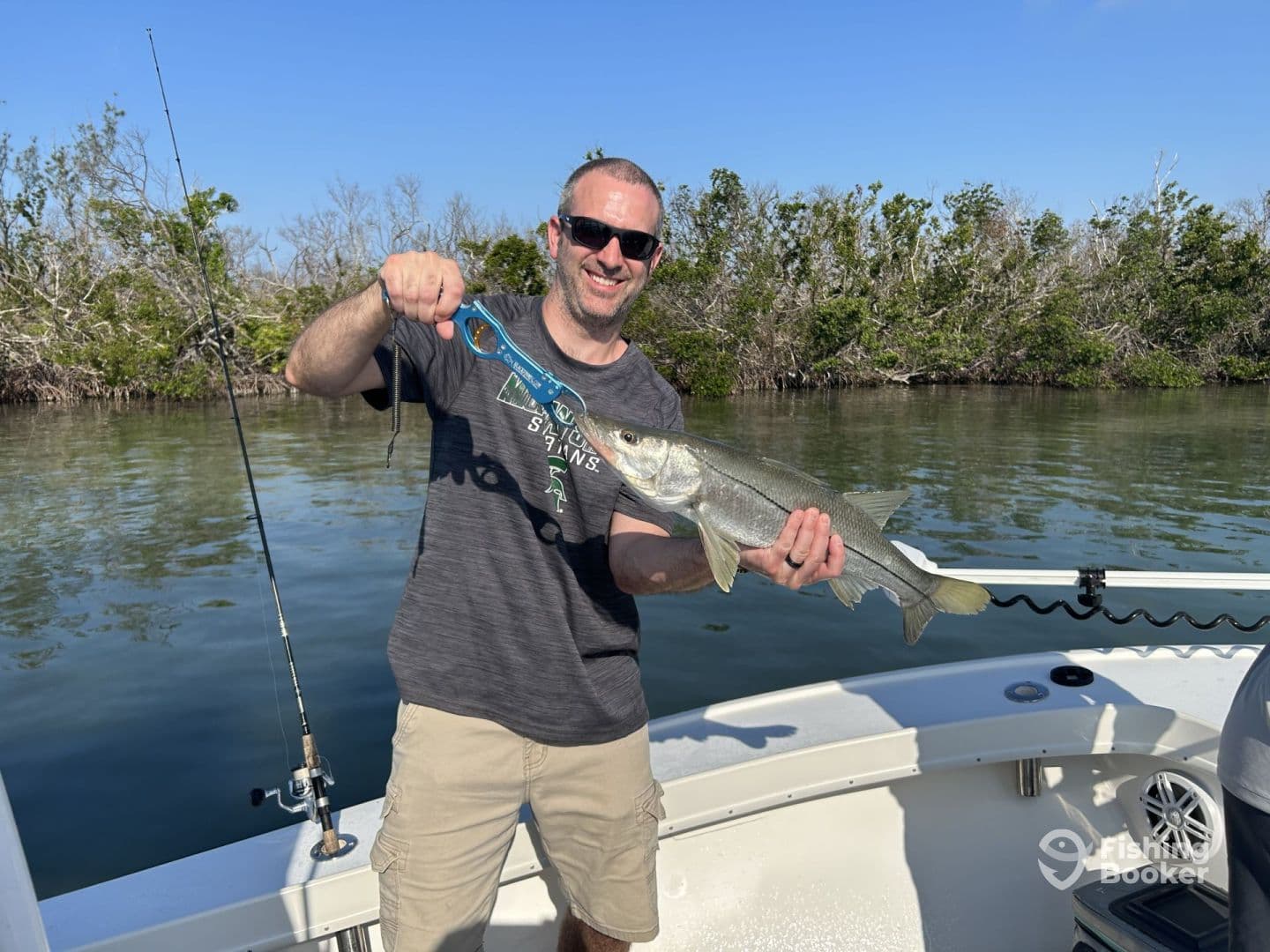 An angler proudly displaying a Snook caught while fishing in a scenic mangrove area.