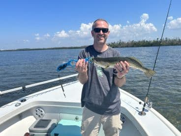 An angler proudly displaying a Speckled Trout while fishing from a boat in a calm waterway.