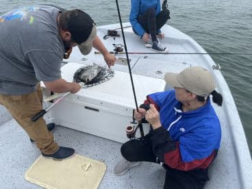 A group of anglers actively fishing on a boat, with one person using a net to handle a caught fish while another prepares their rod.