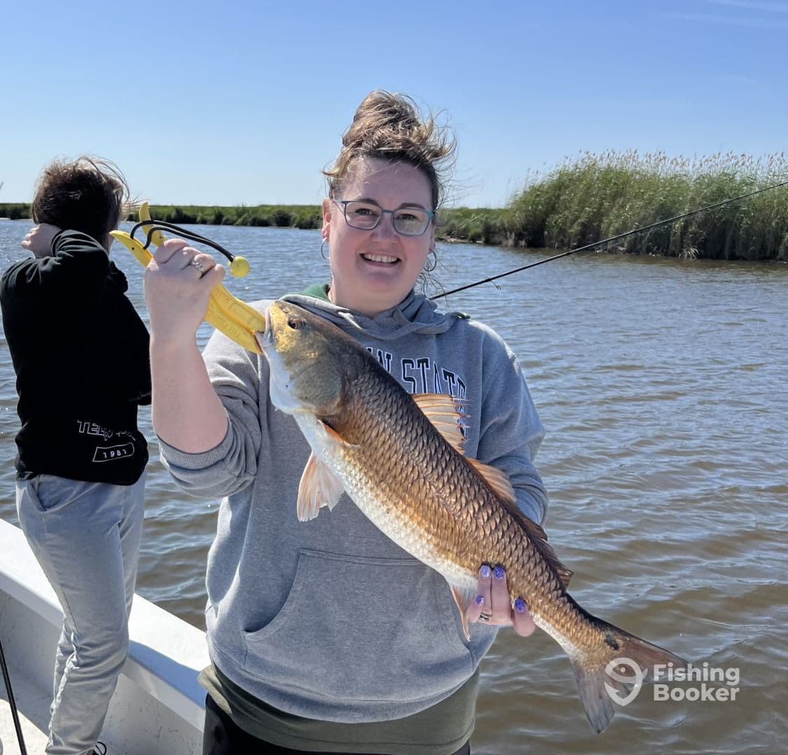 An angler proudly displaying a large Redfish while fishing in a scenic waterway, showcasing a successful day on the water.