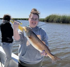 An angler proudly displaying a large Redfish while fishing in a scenic waterway, showcasing a successful day on the water.