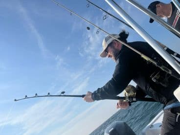 Angler actively reeling in a catch while fishing on a boat, showcasing the excitement of deep-sea fishing.
