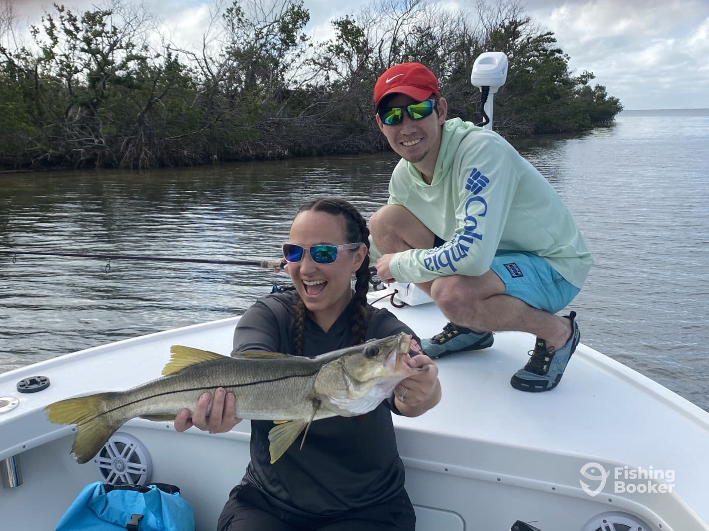 Angler proudly displaying a Snook while fishing on a boat in a scenic coastal environment.