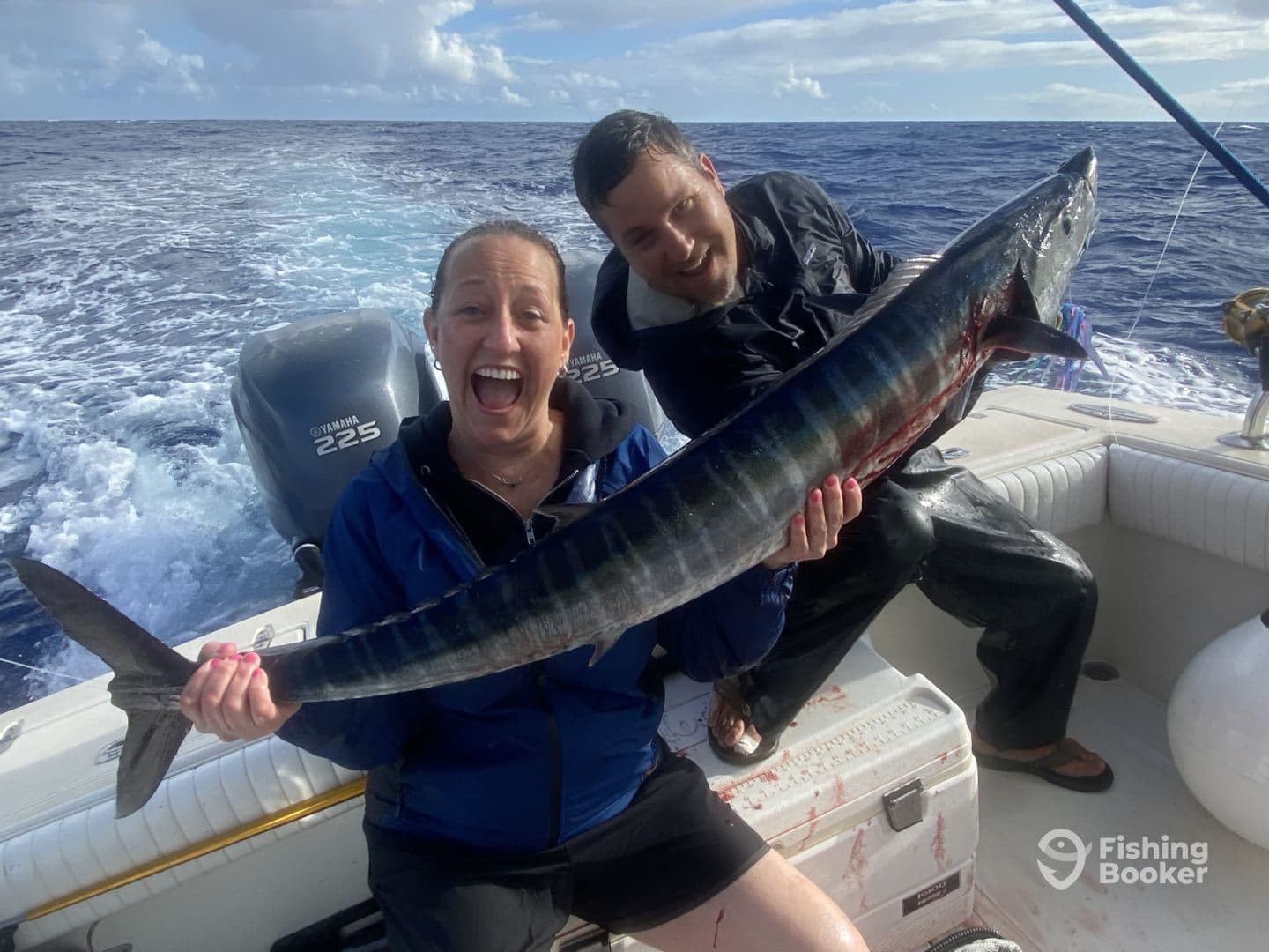 Excited anglers displaying a large Wahoo on a sport fishing boat, showcasing the thrill of deep-sea fishing.