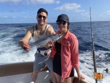 Two anglers proudly displaying a Barracuda while fishing offshore, enjoying a sunny day on the water.
