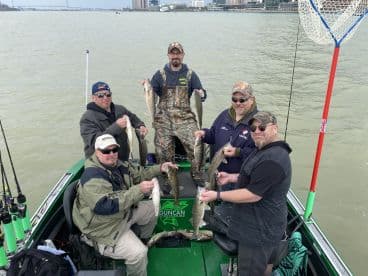 Group of anglers proudly displaying their catch of Walleye while fishing from a boat on a river.