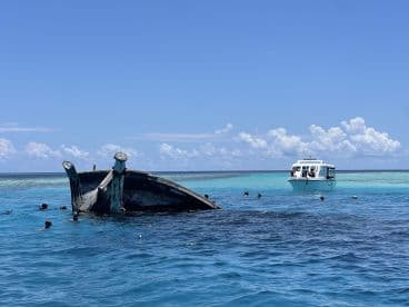 A scenic view of a sunken boat with divers exploring the area, while another fishing boat is anchored nearby in clear turquoise waters.