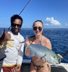 Two anglers proudly displaying a large Bluefin Trevally while fishing in clear blue waters, showcasing a vibrant tropical fishing experience.
