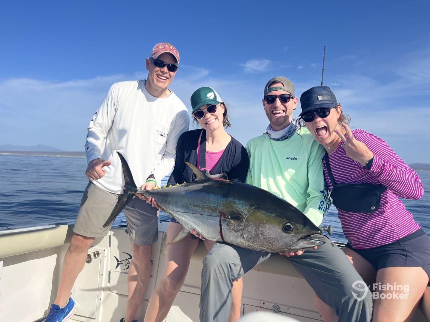 A group of four anglers proudly displaying a large Yellowfin Tuna aboard a fishing boat, enjoying a successful day on the water.