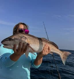 An angler proudly displaying a large Redfish while fishing offshore, showcasing a beautiful day on the water.