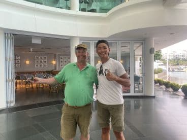 Two anglers posing together in a restaurant setting, with a marina view in the background.