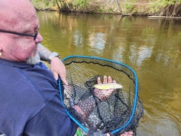 An angler proudly displaying a small fish caught while fishing in a serene river setting.
