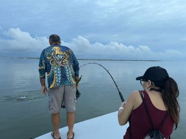 Two anglers engaged in fishing on a calm waterway, showcasing the excitement of reeling in a catch.