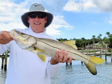 An angler proudly displaying a large Snook caught during a fishing trip, with a scenic waterfront backdrop.