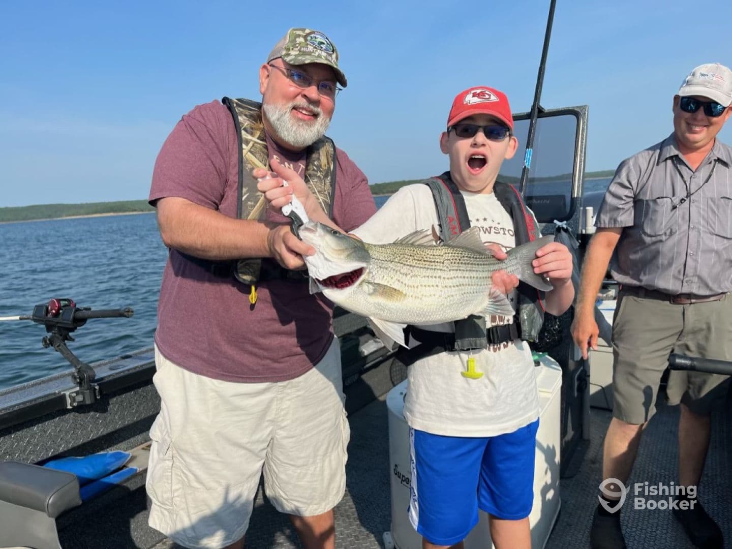 A young angler and an adult proudly displaying a large Striped Bass on a fishing boat, showcasing a successful day on the water.