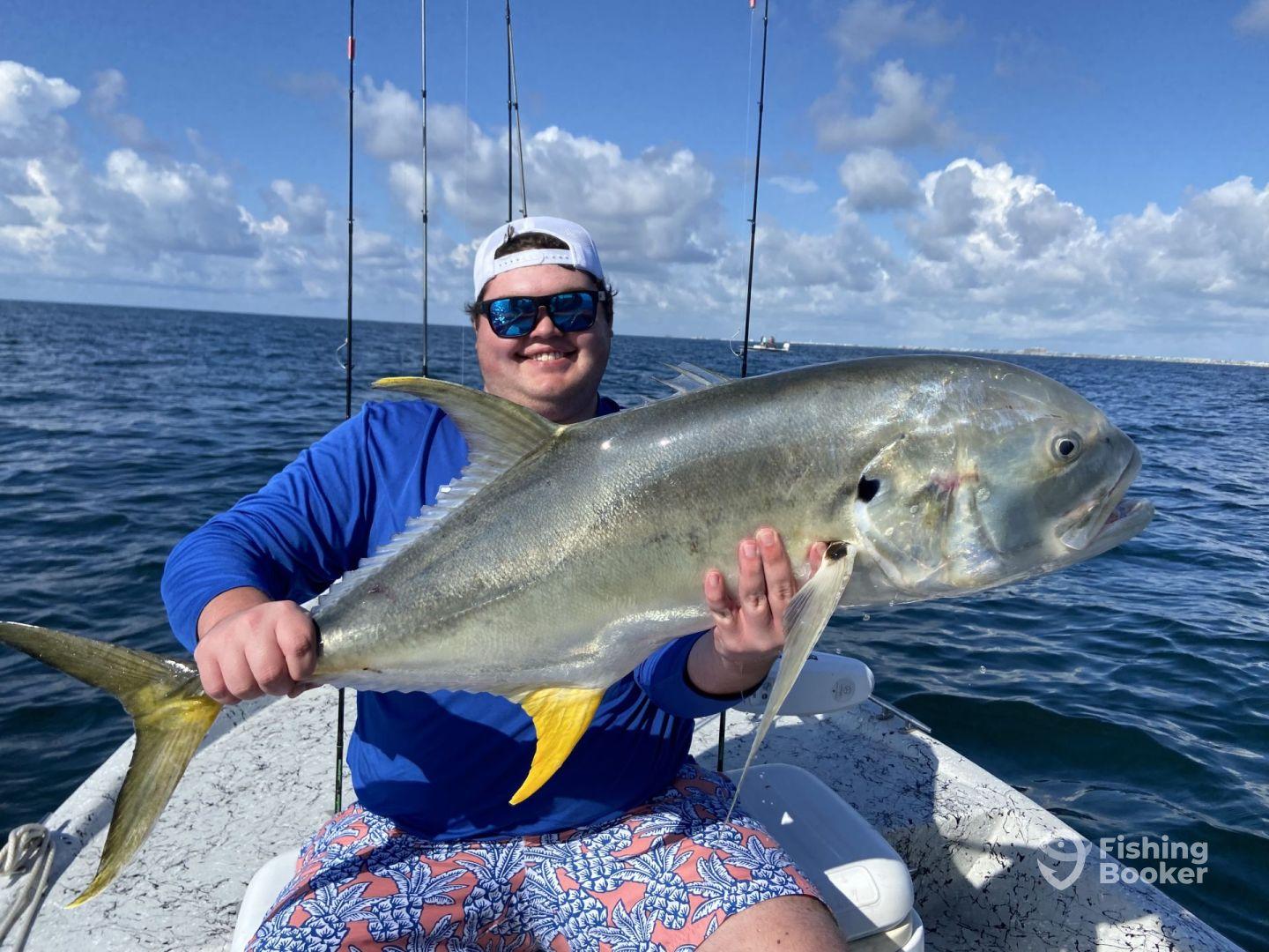 Angler proudly displaying a large Jack Crevalle while fishing on a boat in clear blue waters.