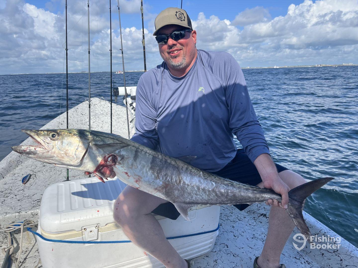 Angler proudly displaying a large King Mackerel while fishing on a boat in open waters.