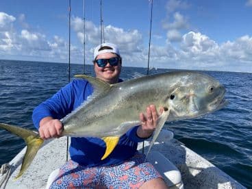 Angler proudly displaying a large Jack Crevalle while fishing on a boat in clear blue waters.