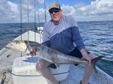 Angler proudly displaying a large King Mackerel while fishing on a boat in open waters.