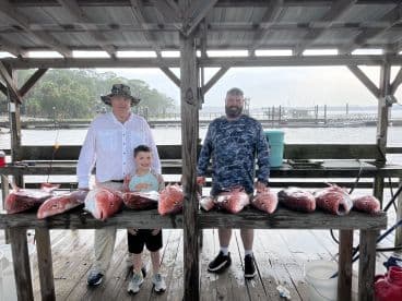 A group of anglers proudly displaying their catch of Red Snapper on a dock after a successful fishing trip.