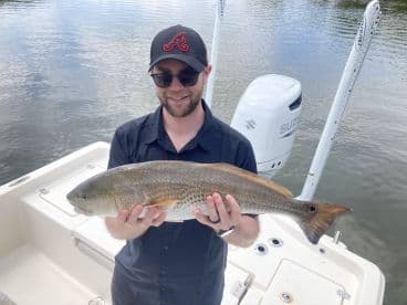 Angler proudly displaying a large Redfish while on a boat, showcasing a successful day of fishing.