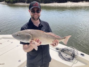 Angler proudly displaying a large Redfish while on a boat in a scenic waterway.