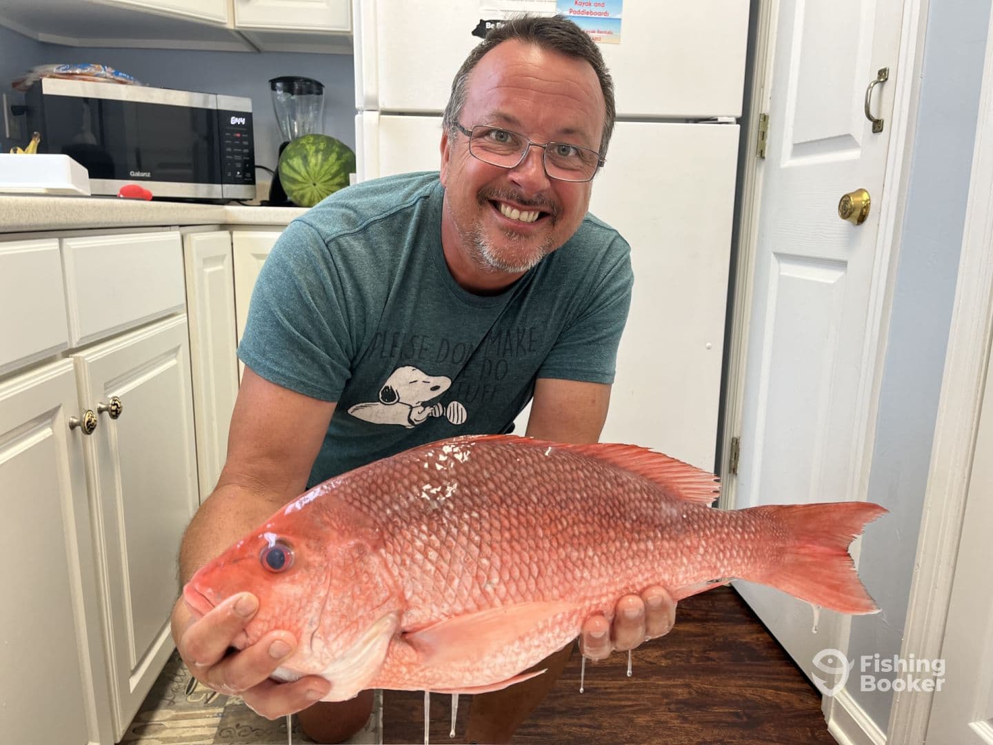 An enthusiastic angler proudly displaying a large Red Snapper in a kitchen setting after a successful fishing trip.