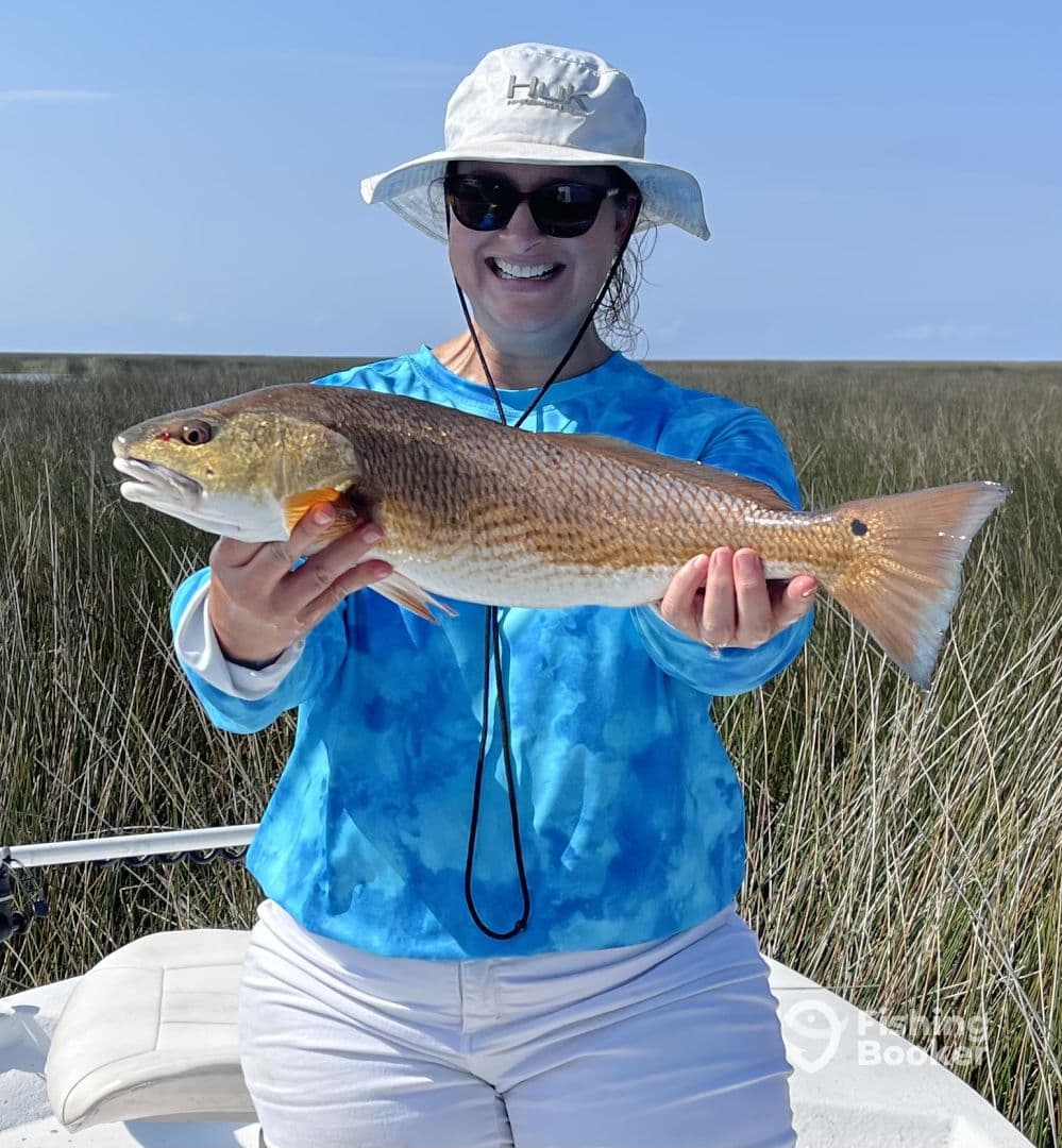 An angler proudly displaying a large Redfish while fishing in a grassy coastal area.