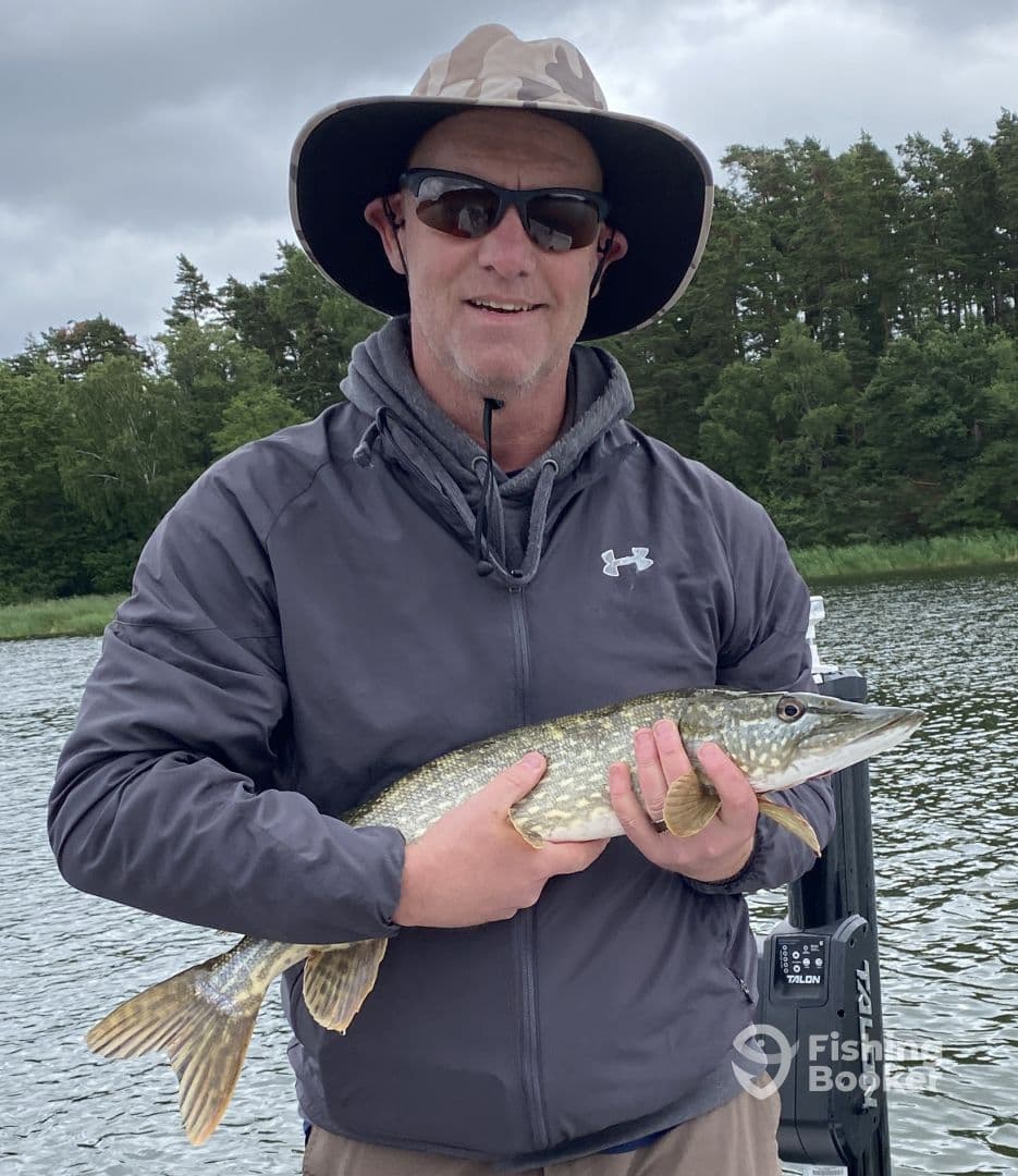 Angler proudly displaying a Northern Pike while fishing in a scenic freshwater environment.