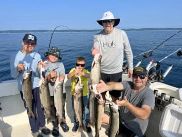 A group of young anglers proudly displaying their catch of Lake Trout while fishing on a boat, showcasing a fun family fishing experience.