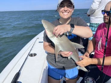 An angler proudly displaying a caught shark while fishing on a boat, showcasing a fun day on the water.