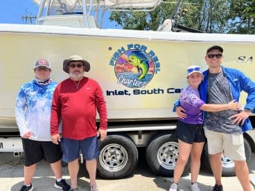 A family poses in front of the 'Fish For Reel Charters' boat in Inlet, South Carolina, showcasing their excitement for a day of fishing.